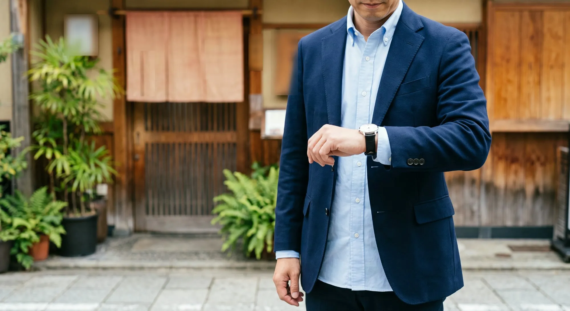 昼間、飲食店の入口の前で腕時計を見て時間を確認する男性