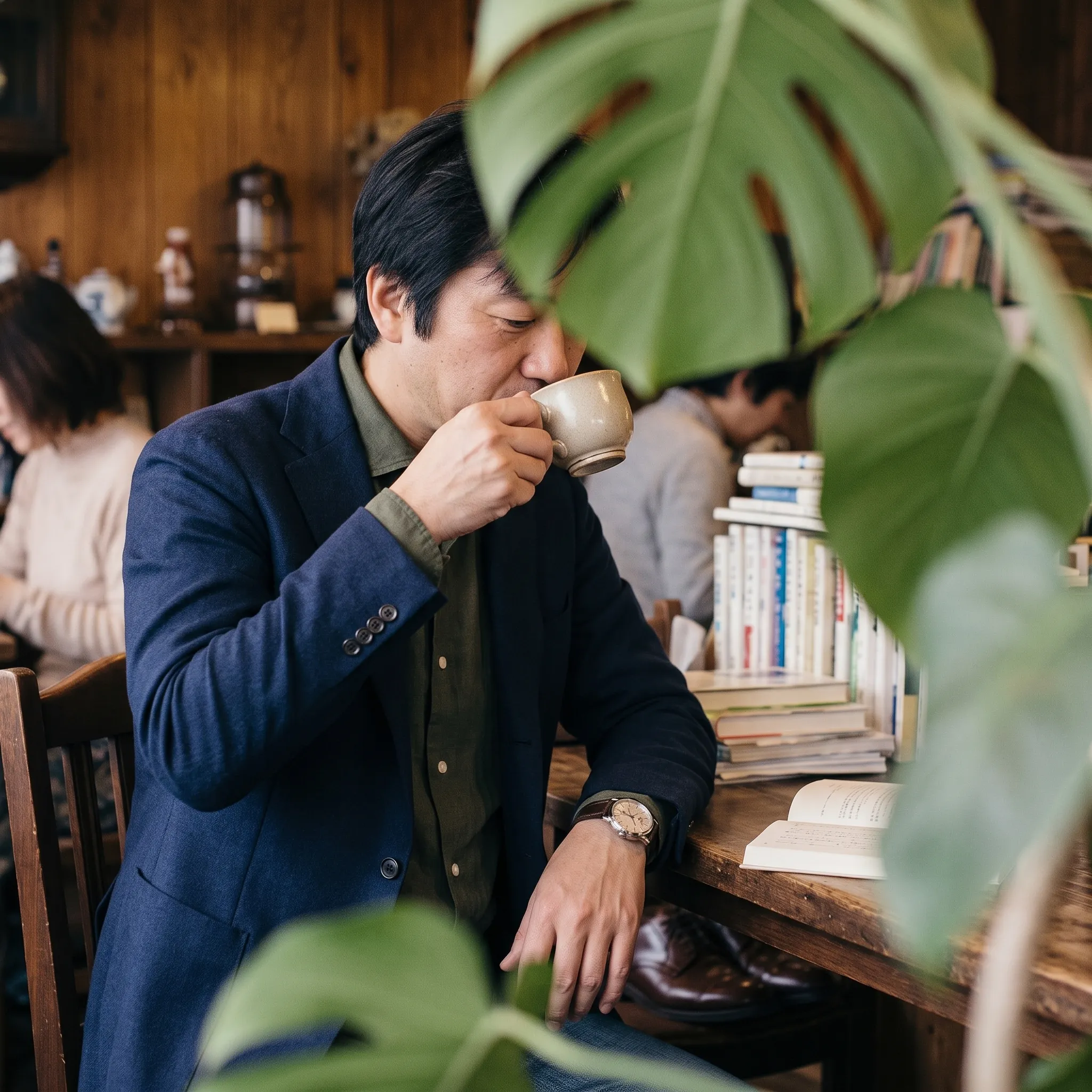 横を向き視線を落としてカップに口をつける男性。手前に観葉植物の葉がぼけて入っている